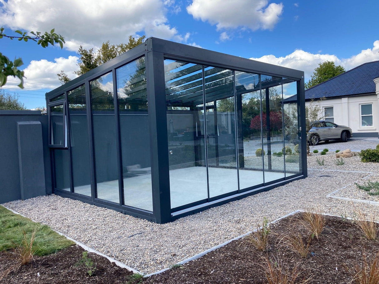 Modern glass garden room with black frame in landscaped outdoor setting
