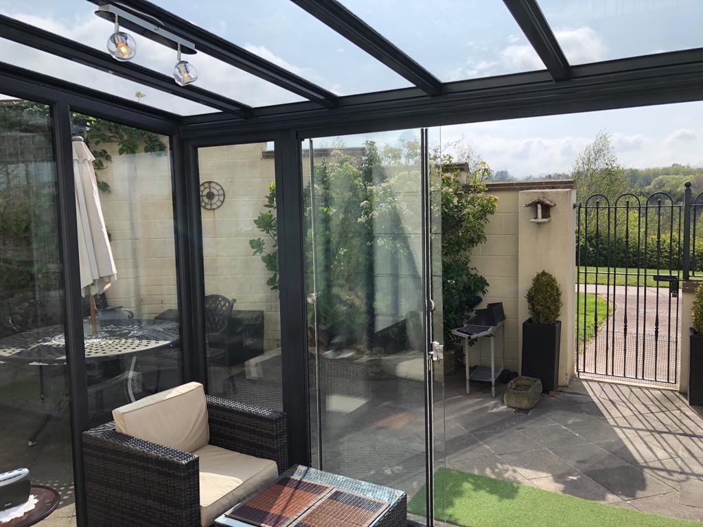Modern glass garden room with black frame, outdoor seating, and patio view