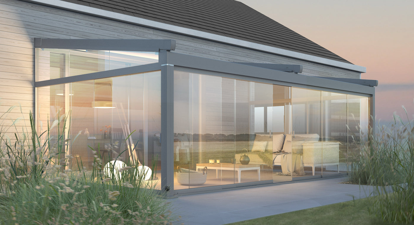 Modern glass garden room with cozy seating area attached to a house at sunset