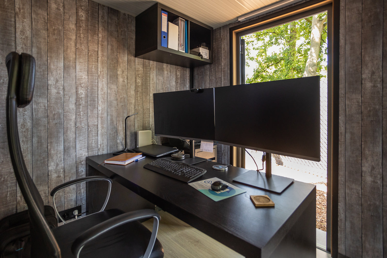 Modern home office setup with dual monitors, ergonomic chair, and garden view through window