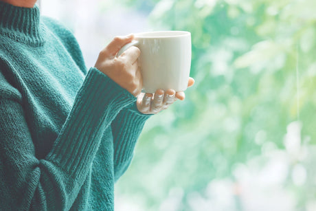 Cozy moment with a white mug in a green sweater, enjoying garden views