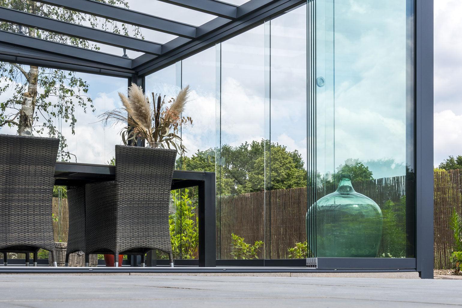 Modern glass veranda with wicker chairs and greenery, perfect for outdoor living spaces.