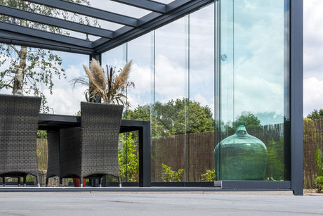 Modern glass veranda with wicker chairs and greenery, perfect for outdoor living spaces.