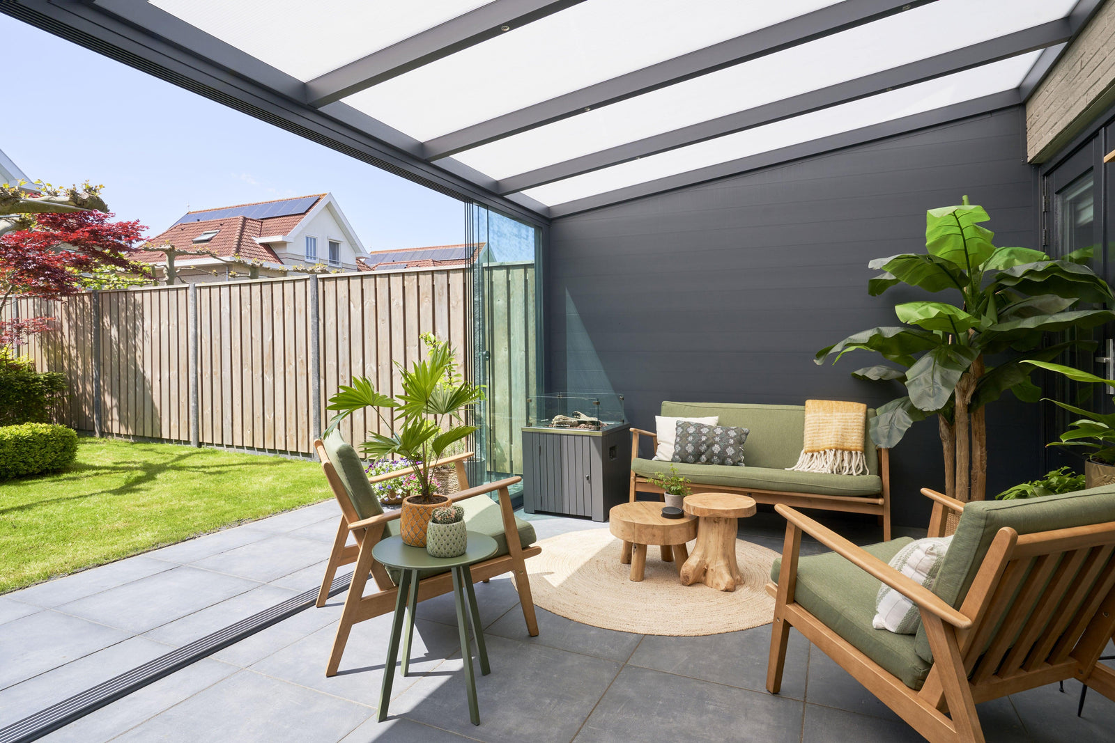 Modern garden veranda with green seating, wooden tables, and lush plants under a sleek canopy