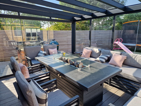 Modern outdoor veranda with glass roof, gray lounge seating, and fire table for cozy garden living