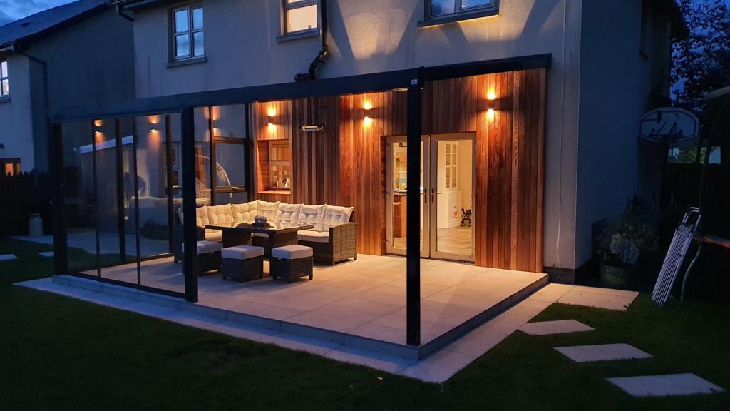 Modern garden veranda with cozy seating, warm lighting, and glass walls for outdoor living comfort.