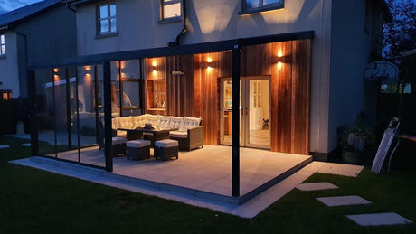 Modern garden veranda with cozy seating, warm lighting, and glass walls for outdoor living comfort.