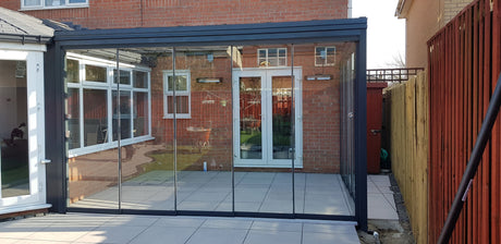 Modern glass veranda with black frame, enhancing outdoor living space beside brick home