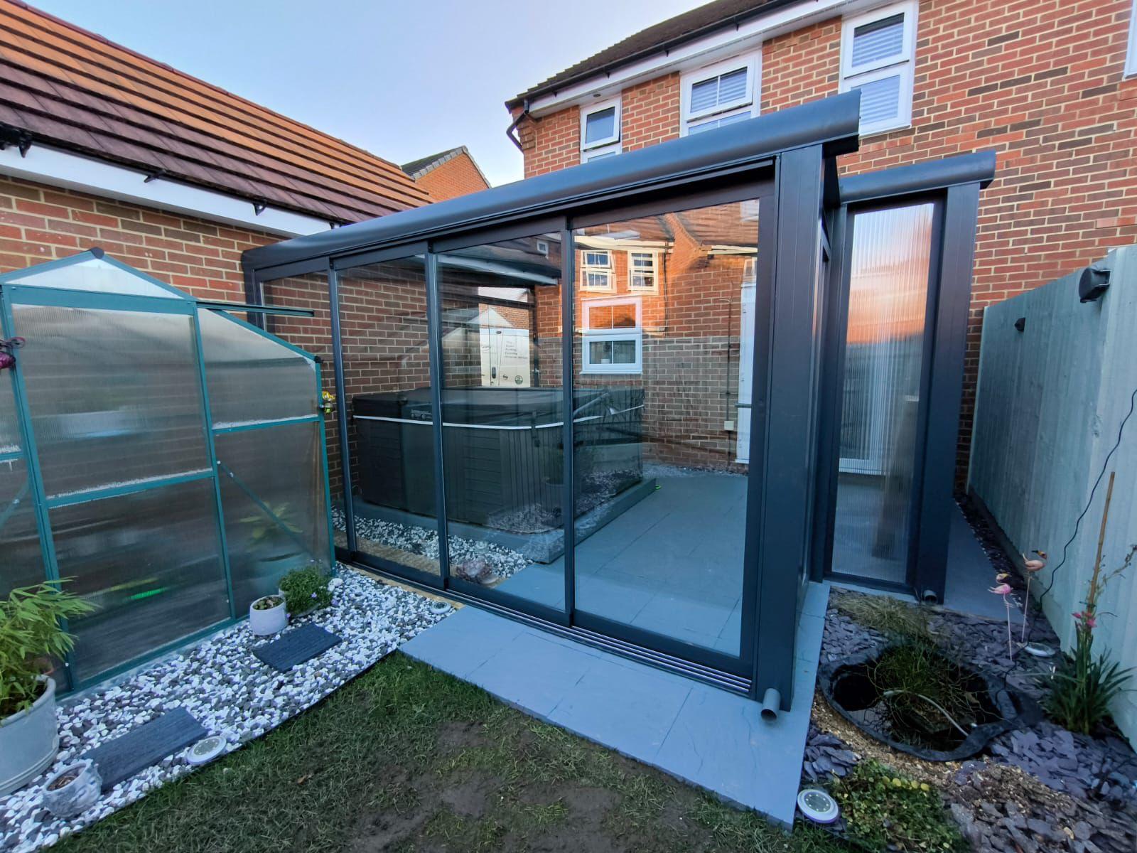 Modern glass garden room with hot tub, sleek black frame, and brick backdrop for outdoor luxury living.