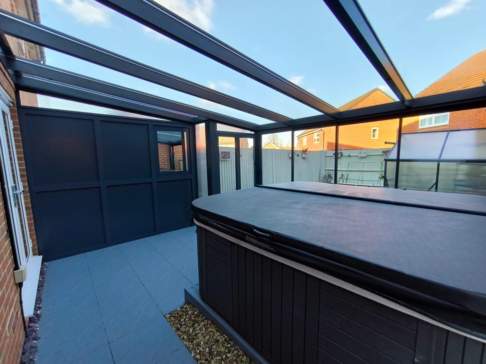 Modern outdoor hot tub under glass roof with sleek black panels and tiled flooring