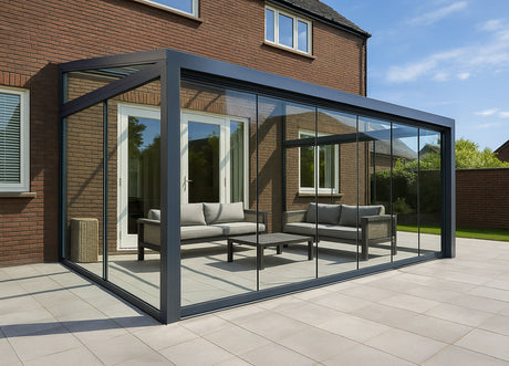 Modern glass garden room with black frame, outdoor sofa set, attached to brick home on sunny patio