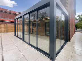 Modern glass garden room with black frame and sliding doors on tiled patio
